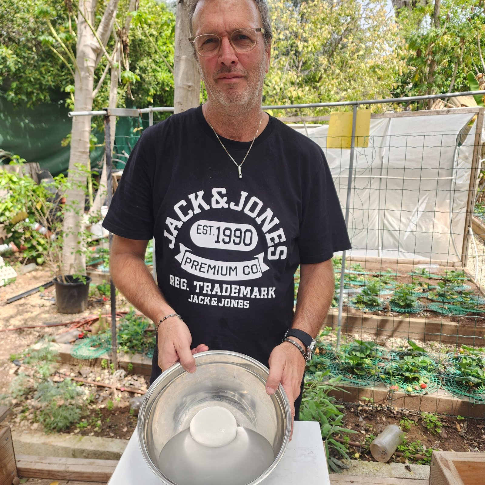 משתתף מציג כדור מוצרלה טרי בעבודת יד מתוך קערת מים קרים, על רקע הבוסתן הירוק בסדנת מוצרלה ב"גבינות ברמות"